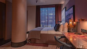 Una habitación de hotel moderna con una cama, un escritorio y vistas de la ciudad a través de amplias ventanas.