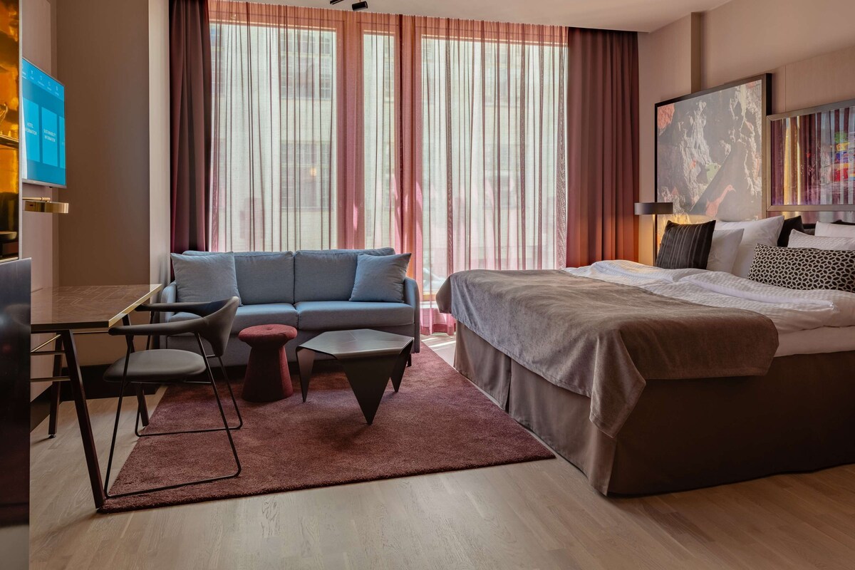Una habitación de hotel moderna con sofá, una mesita, una cama y un televisor.