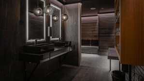 Un baño moderno con paneles de madera oscura, un lavabo negro y tres lámparas colgantes.