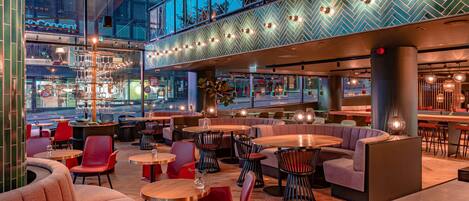 A modern restaurant with a high ceiling, exposed beams, and a mix of seating options including tables and booths.
