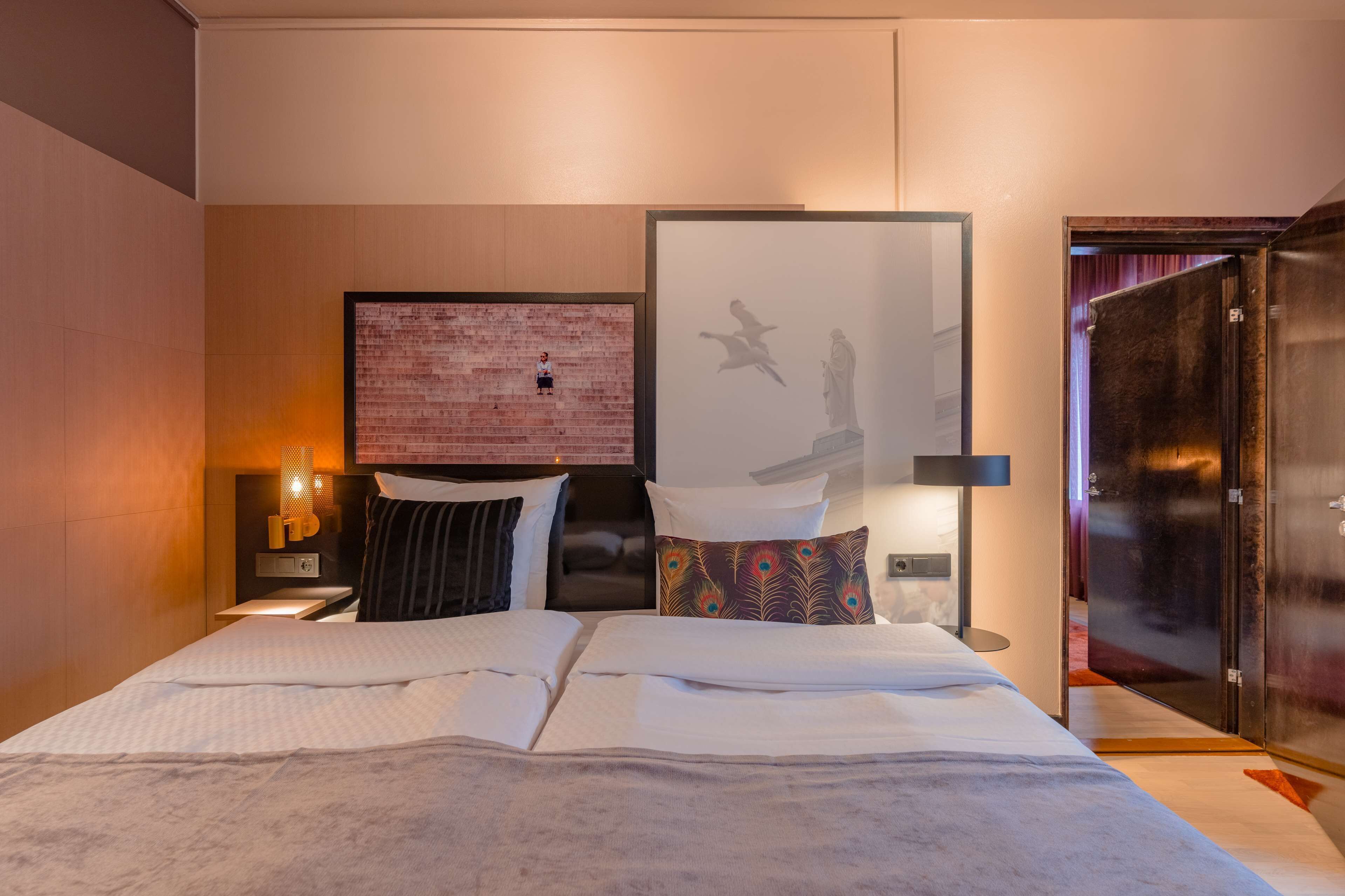 A hotel room with a bed, pillows, a wall-mounted light, and a framed picture.