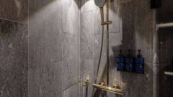 A modern shower with a gold showerhead and control panel, mounted on a textured wall.