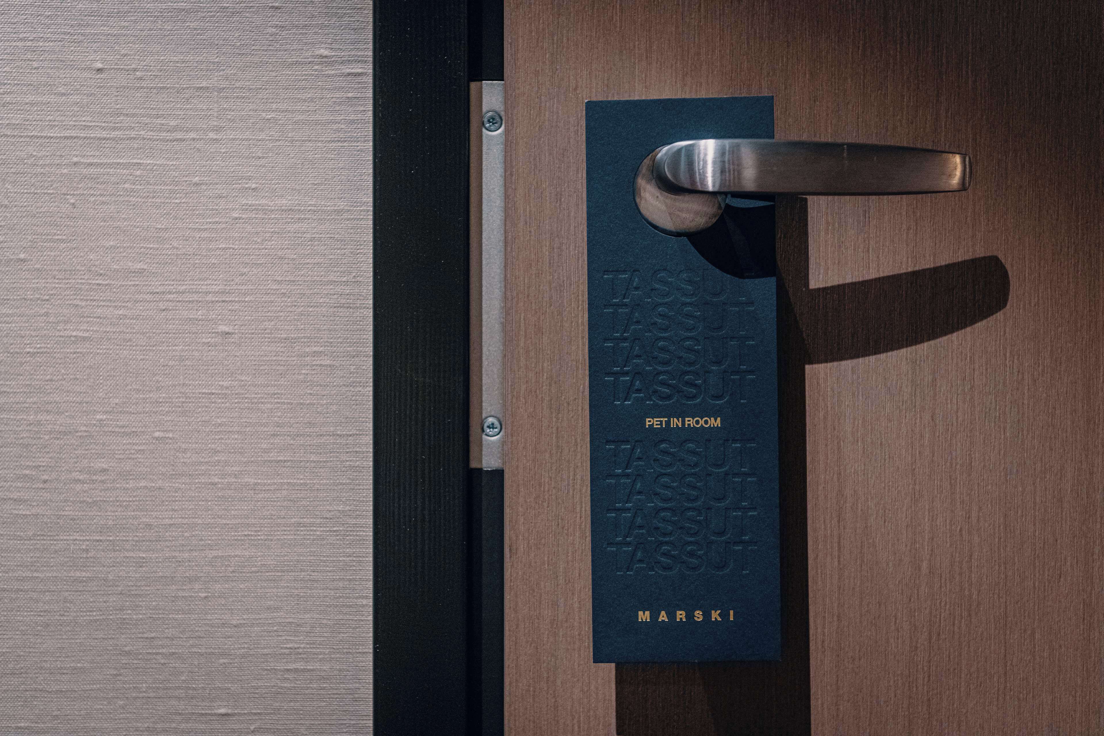 A door with a metal handle and a plaque that reads "TASSU PET IN ROOM" and "MARSKI".