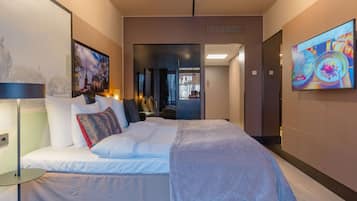 Una camera d'albergo moderna con un letto grande, una TV a schermo piatto fissata al muro e vista sulla città attraverso la finestra.