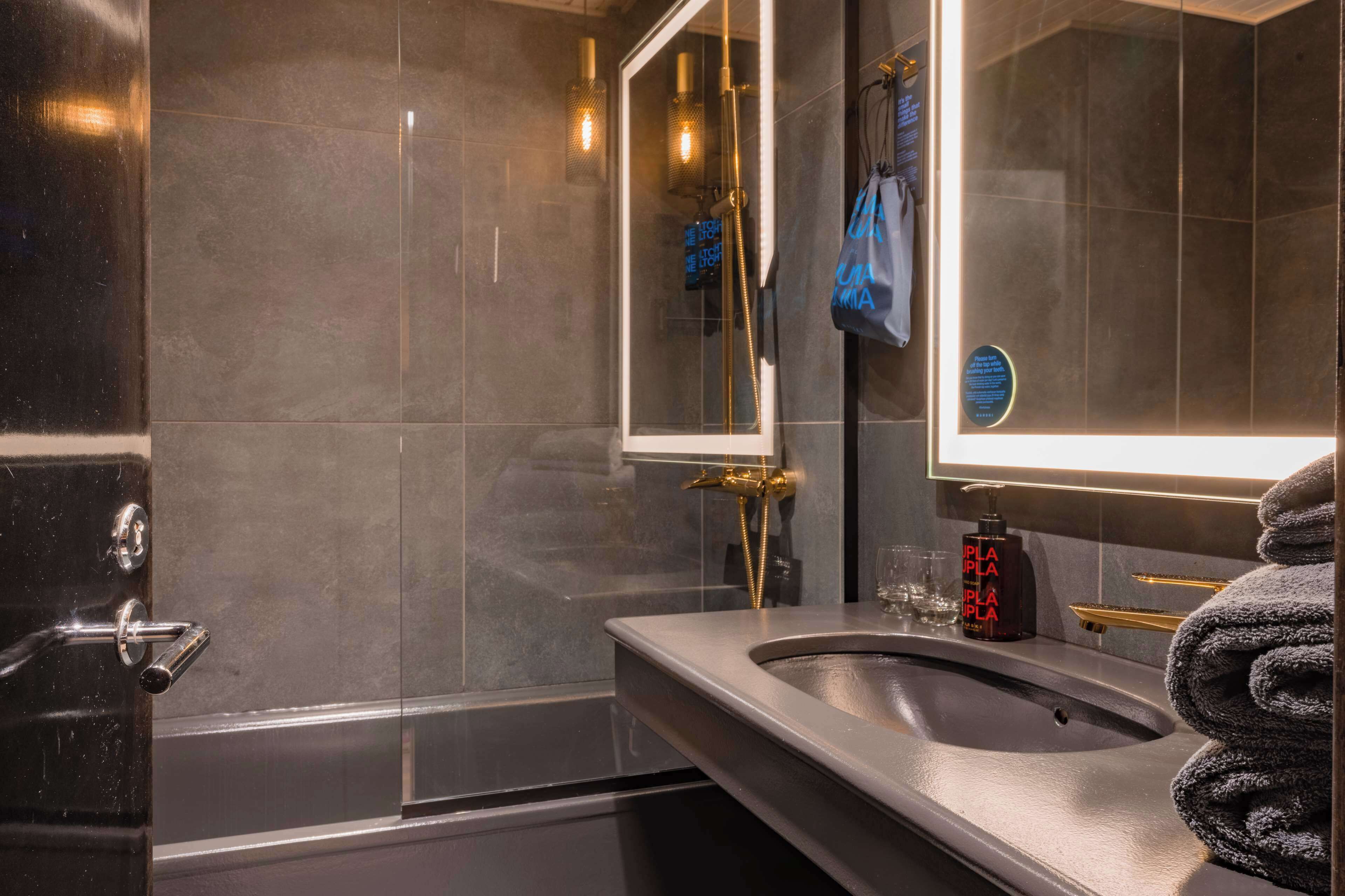 A modern bathroom with a glass-enclosed shower, a sink with a towel rack, and a mirror with a light above it.
