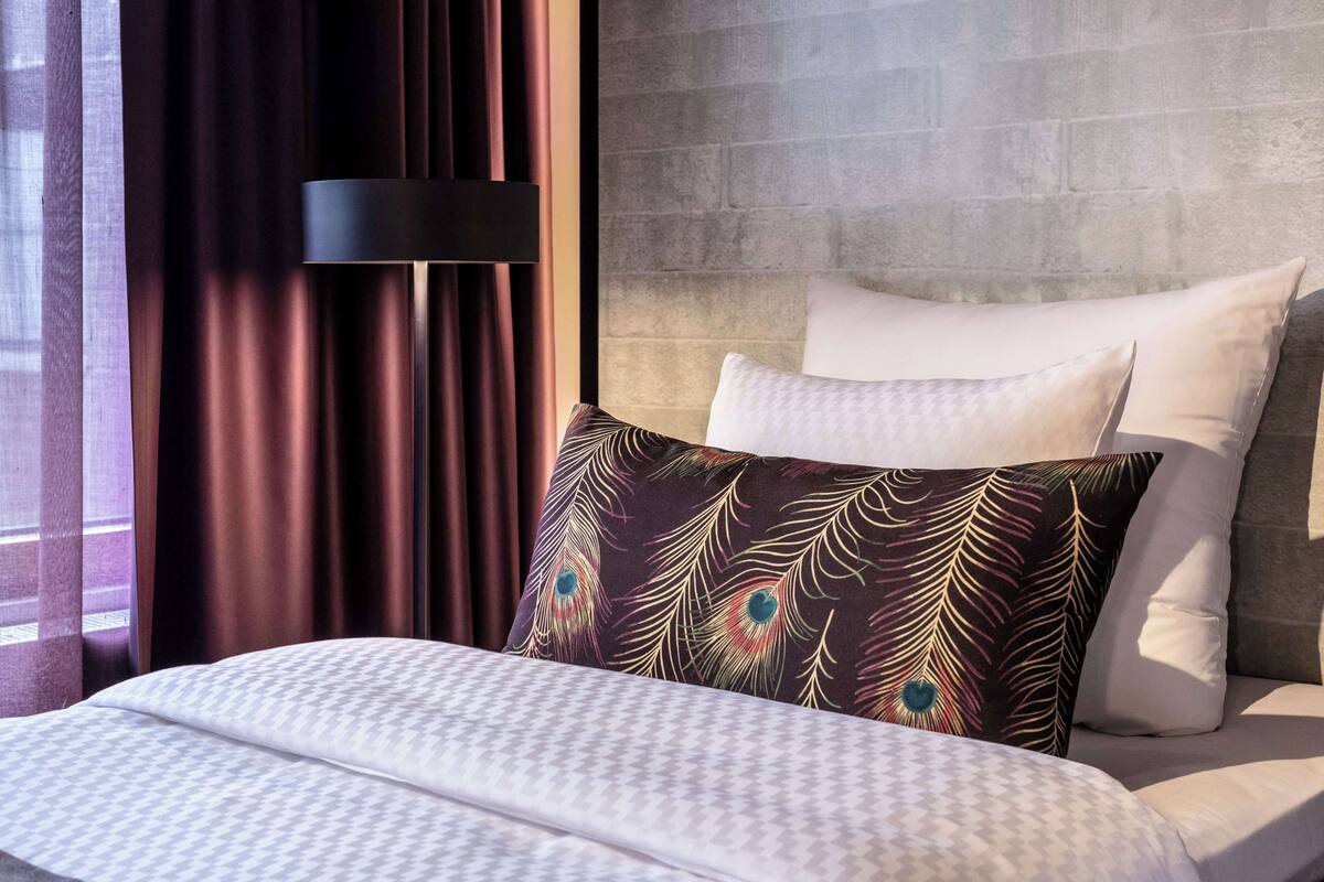 A hotel room with a bed, a headboard, and a window with curtains.