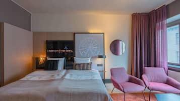 Una habitación de hotel moderna con una cama grande, un televisor, un espejo redondo y dos sillones rosados.