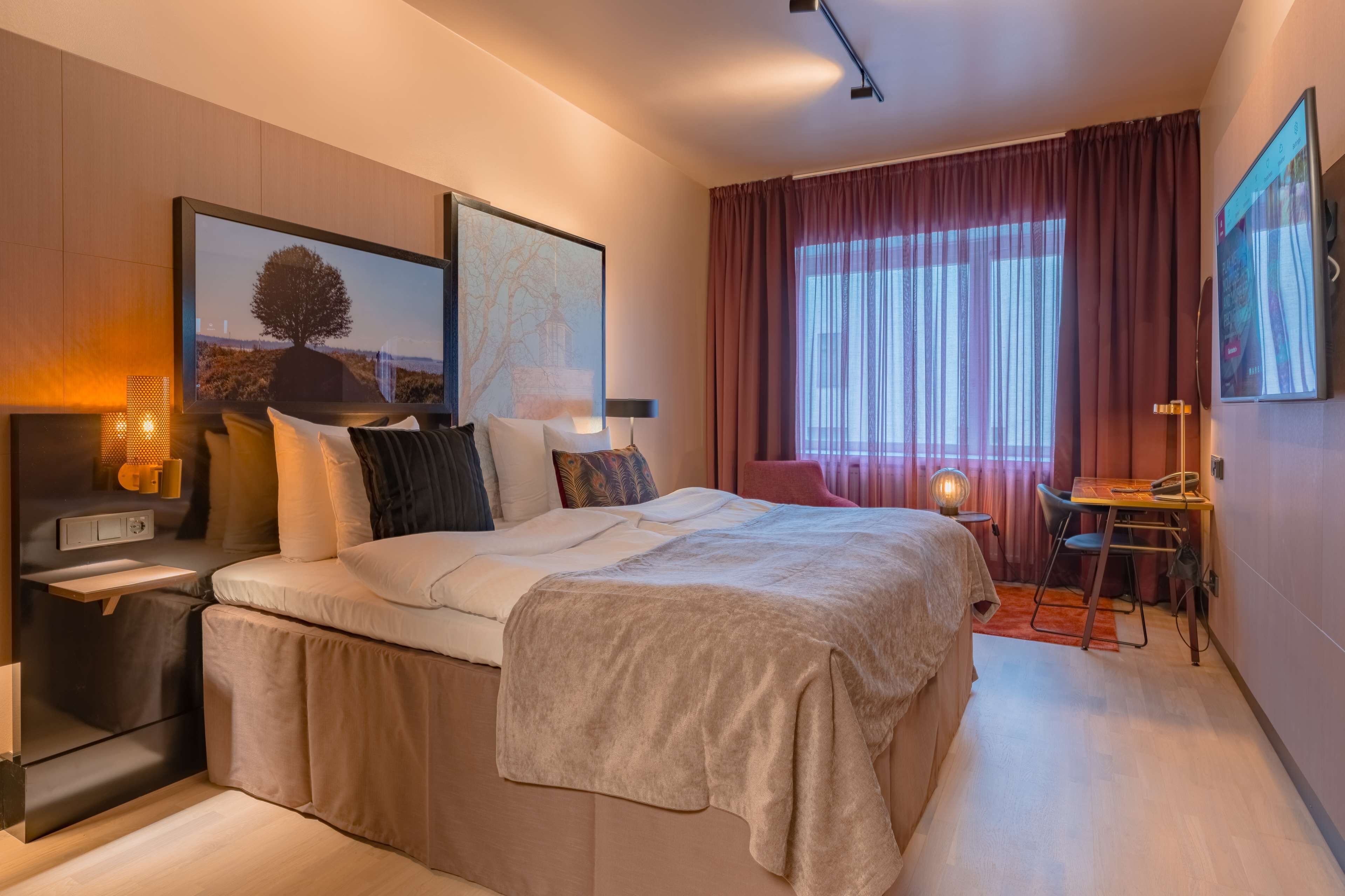 A modern hotel room with a large bed, bedside tables, a desk, and a chair.
