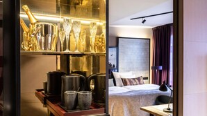 Habitación de hotel con cama, mesita de noche y minibar que contiene varios artículos, incluyendo vasos y una botella.