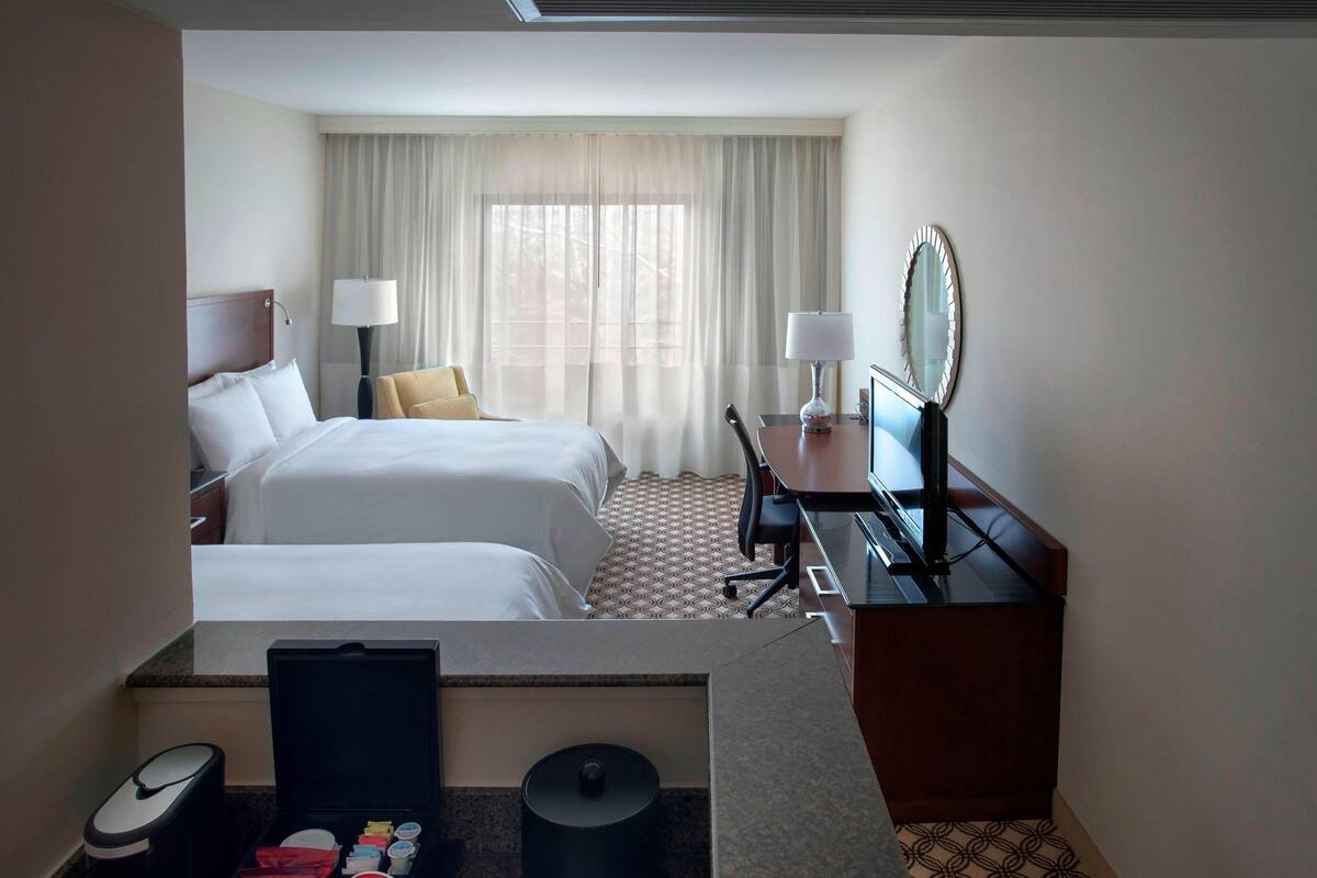 Ein Hotelzimmer mit zwei Betten, einem Schreibtisch mit Spiegel, einem Sessel und einer Schreibtischlampe.