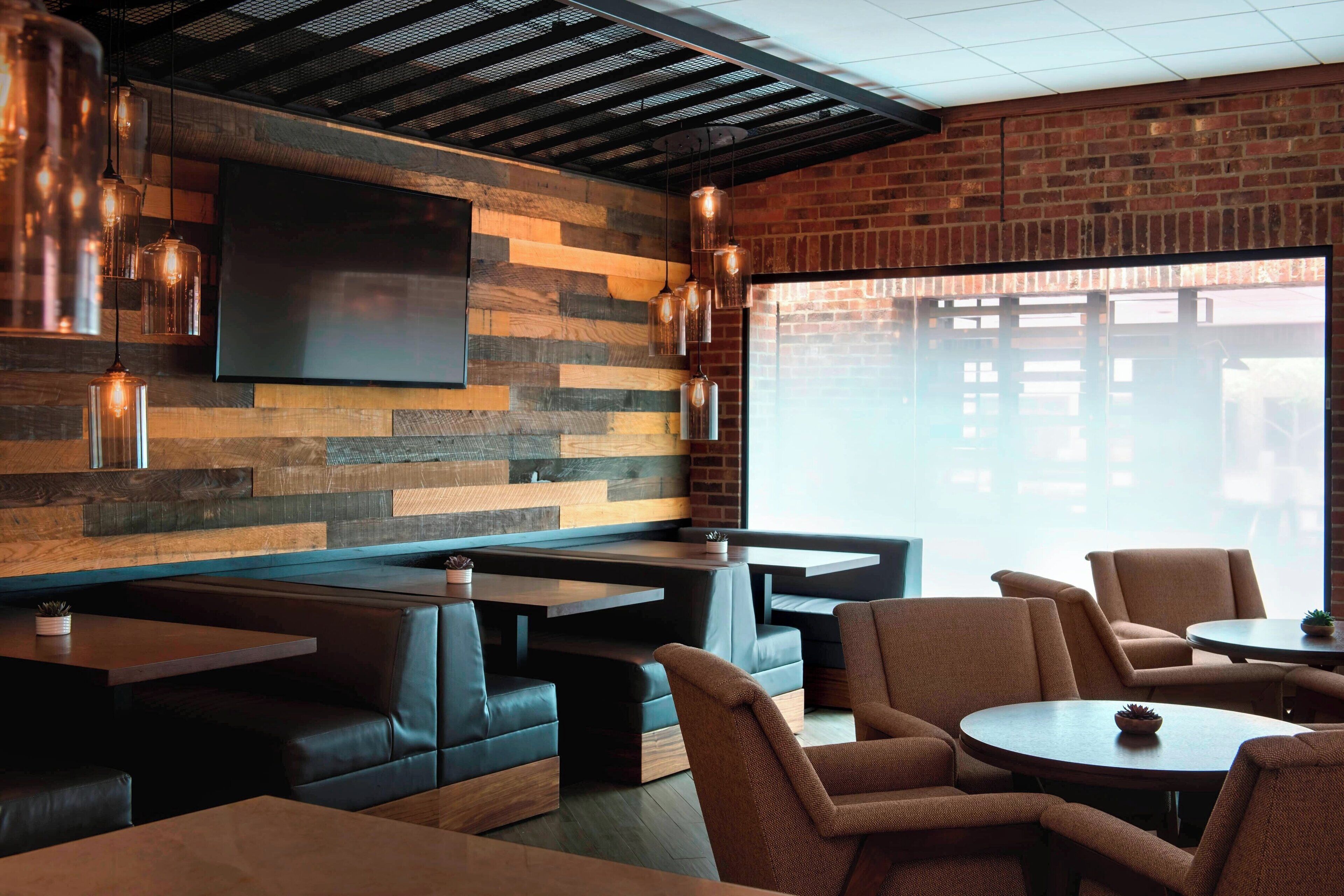Een modern restaurant met houten lambrisering, lederen zitbanken en hangende metalen lampen.