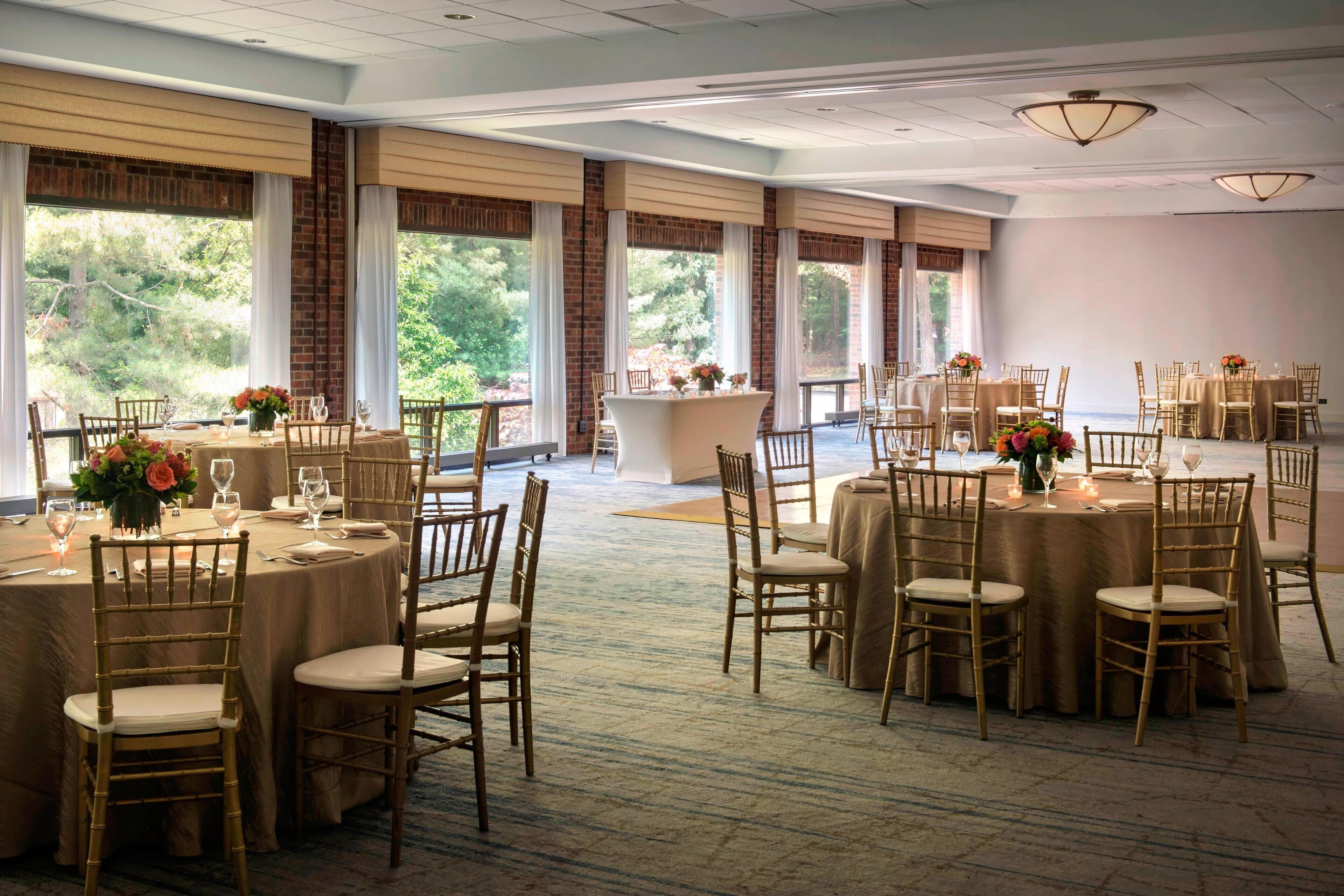 Un salón de banquetes con mesas redondas, sillas y centros de mesa florales.