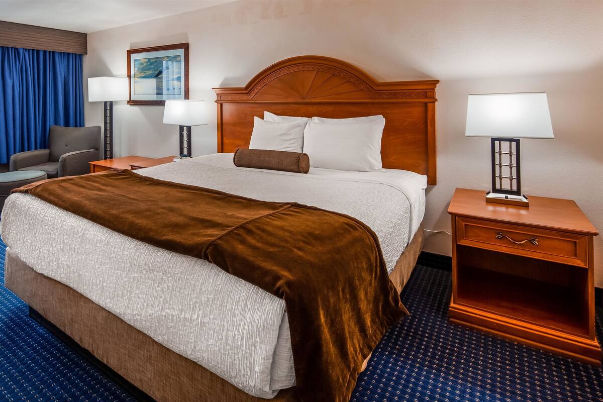 Una habitación de hotel con una cama grande, dos mesitas de noche con lámparas, una silla, un escritorio y una ventana con cortinas azules.