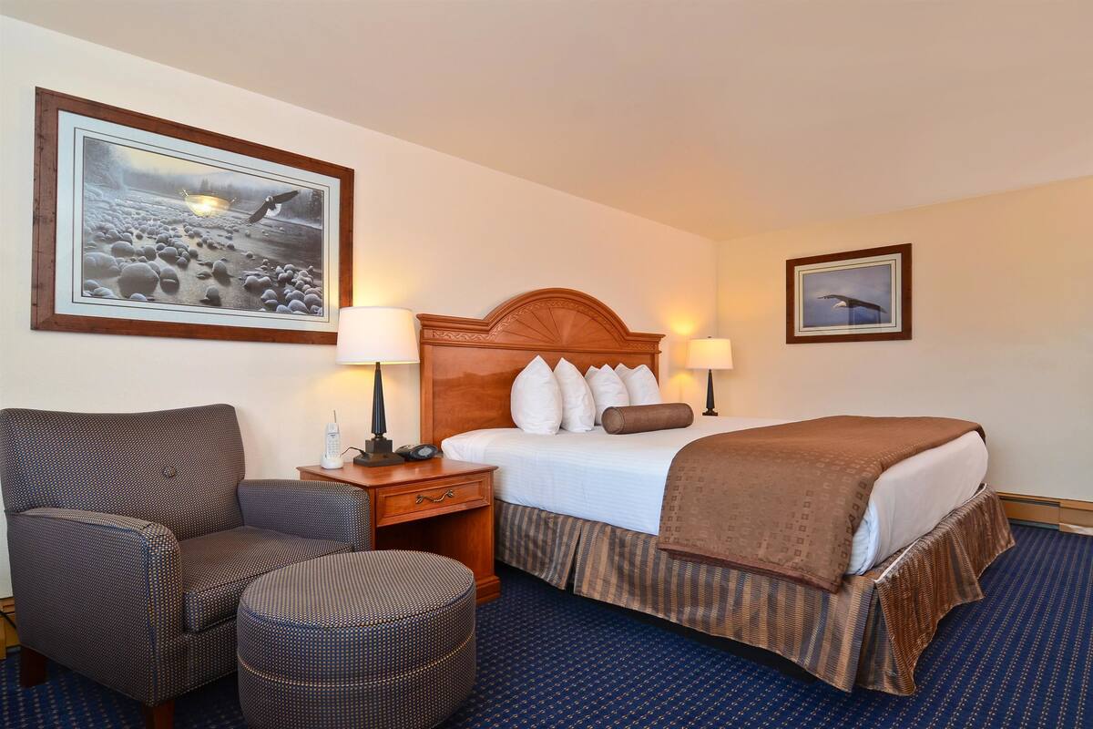 Una habitación de hotel con una cama, una silla, una mesita de noche y dos lámparas fijadas a la pared.