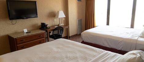 Quarto de hotel com duas camas, uma escrivaninha com luminária, televisão e uma janela com cortinas.