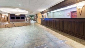 Eine Hotelhalle mit einer Rezeption, einer Treppe und einem gefliesten Boden.