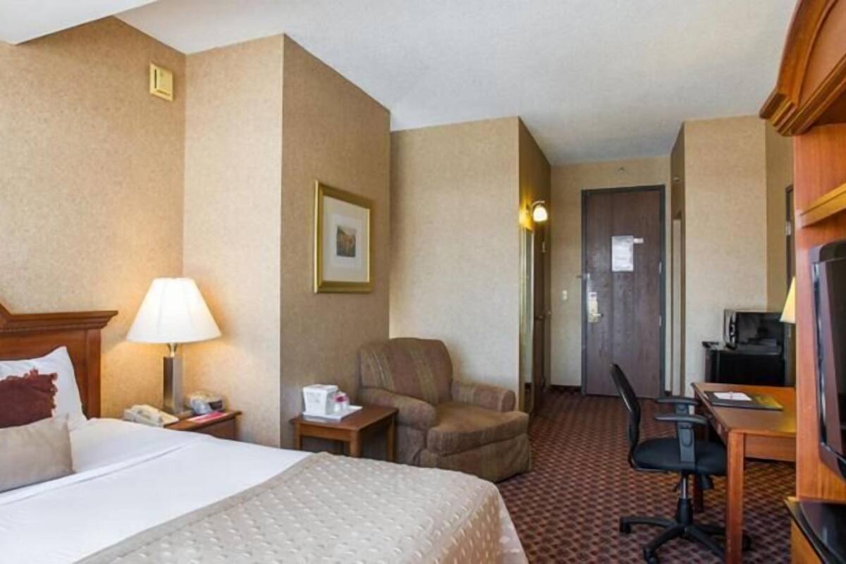 Ein Hotelzimmer mit Bett, Schreibtisch, Sessel, Fernseher und Lampe.