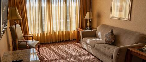 A hotel room with a sofa, a chair, a table, and a large window with curtains.