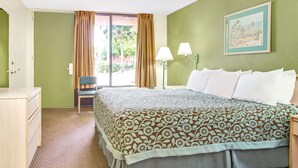 Une chambre d’hôtel avec un lit, une chaise, un bureau et une fenêtre avec des rideaux.