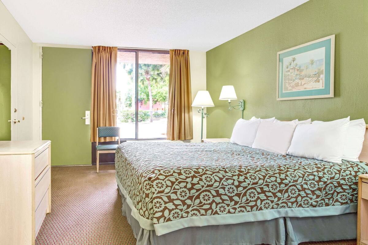 Ein Hotelzimmer mit Bett, Sessel, Schreibtisch, Lampe und einem Bild an der Wand.