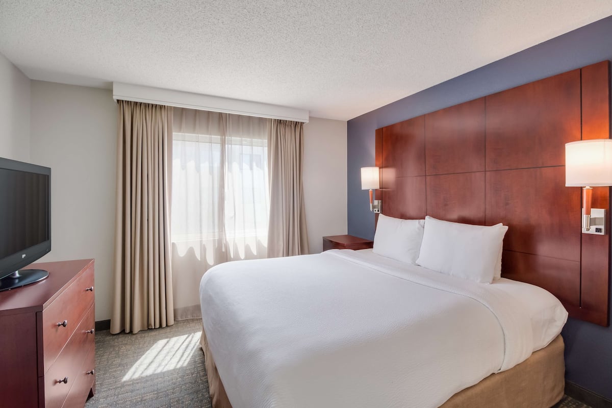 A hotel room with a large bed, a TV on a dresser, and a window with curtains.