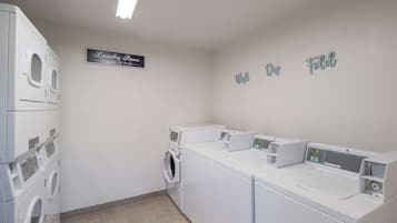 Un lavadero con varias lavadoras blancas, un letrero que dice "Laundry Room Loads of Fun" y decoración de pared con la inscripción "Web My Fold".