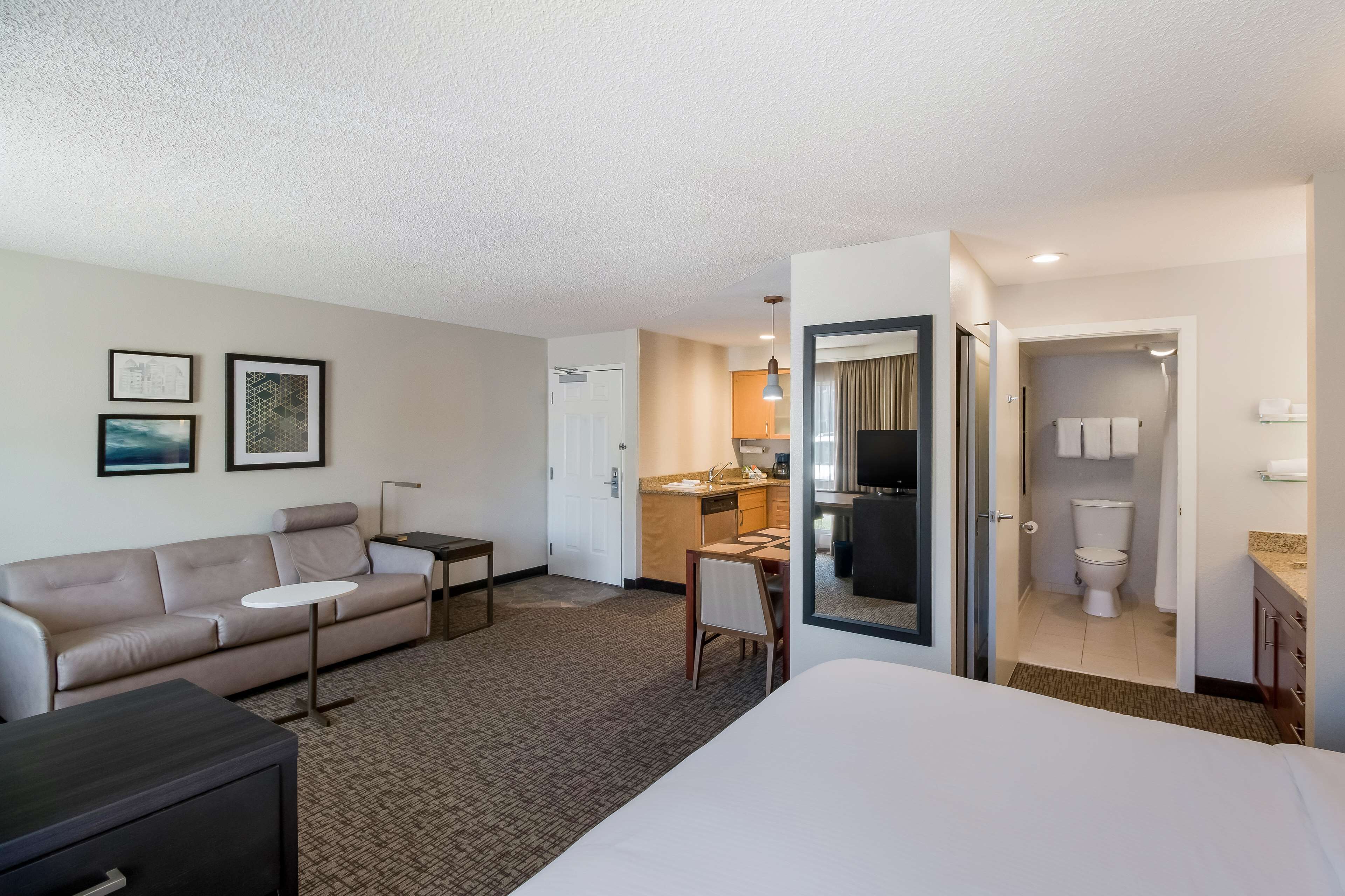 A hotel room with a bed, a sofa, a small table, a desk, and a kitchenette.