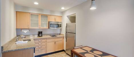 Cocina compacta con armarios de madera, microondas, refrigerador y una mesa de comedor con sillas.