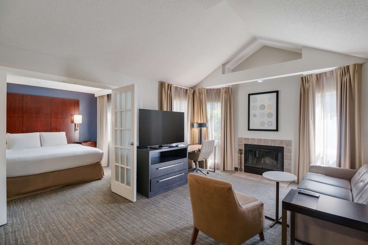 A hotel room with a bed, a desk with a TV, a sofa, a chair, and a fireplace.