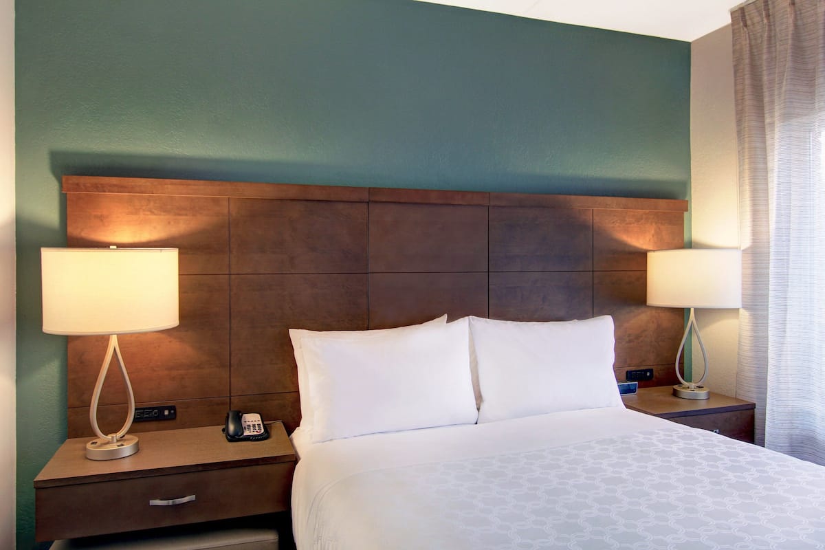 Une chambre d’hôtel avec un grand lit, deux tables de chevet avec des lampes, un téléphone et un tiroir de commode.
