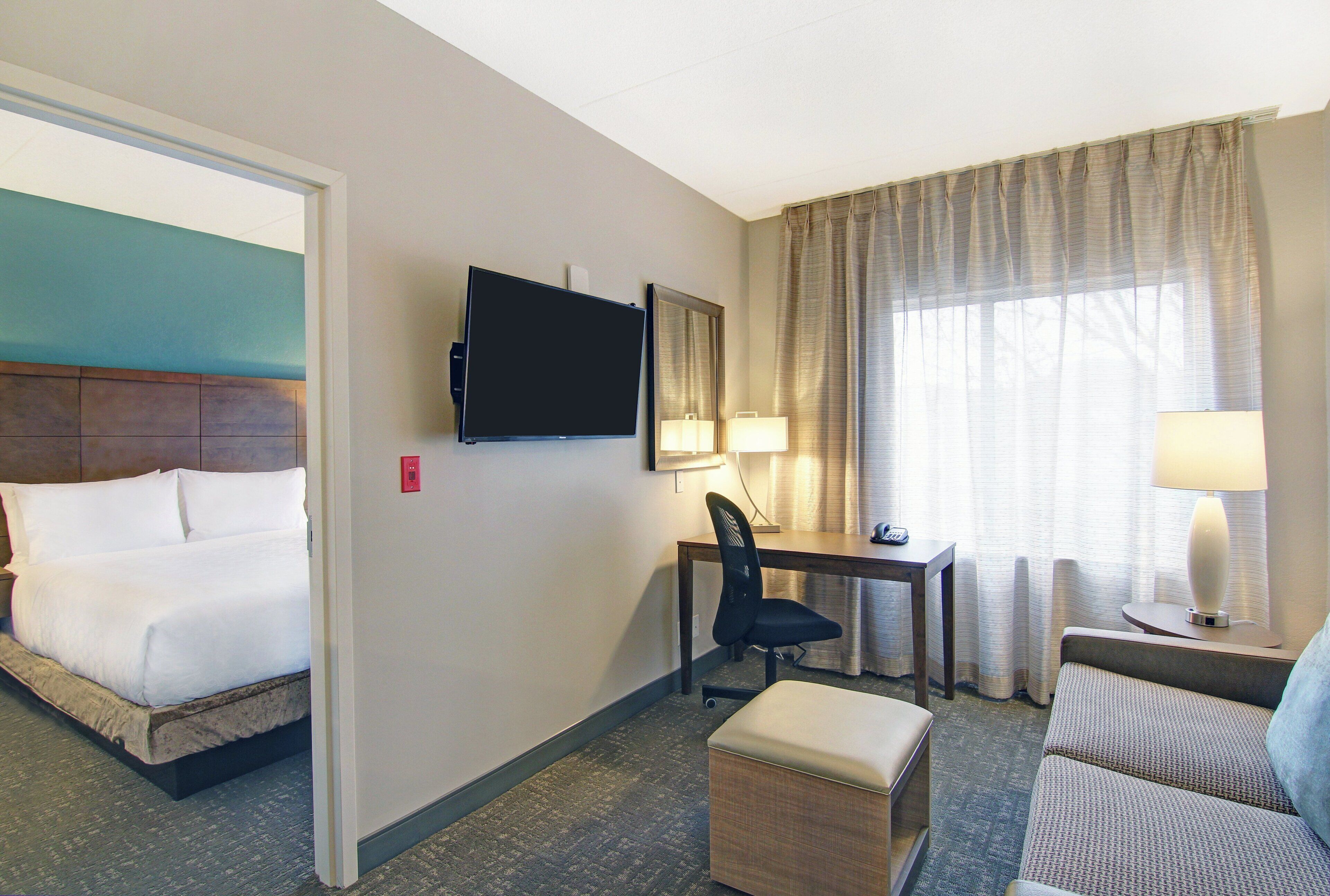 A hotel room with a bed, a desk, a chair, a television, and a window with curtains.