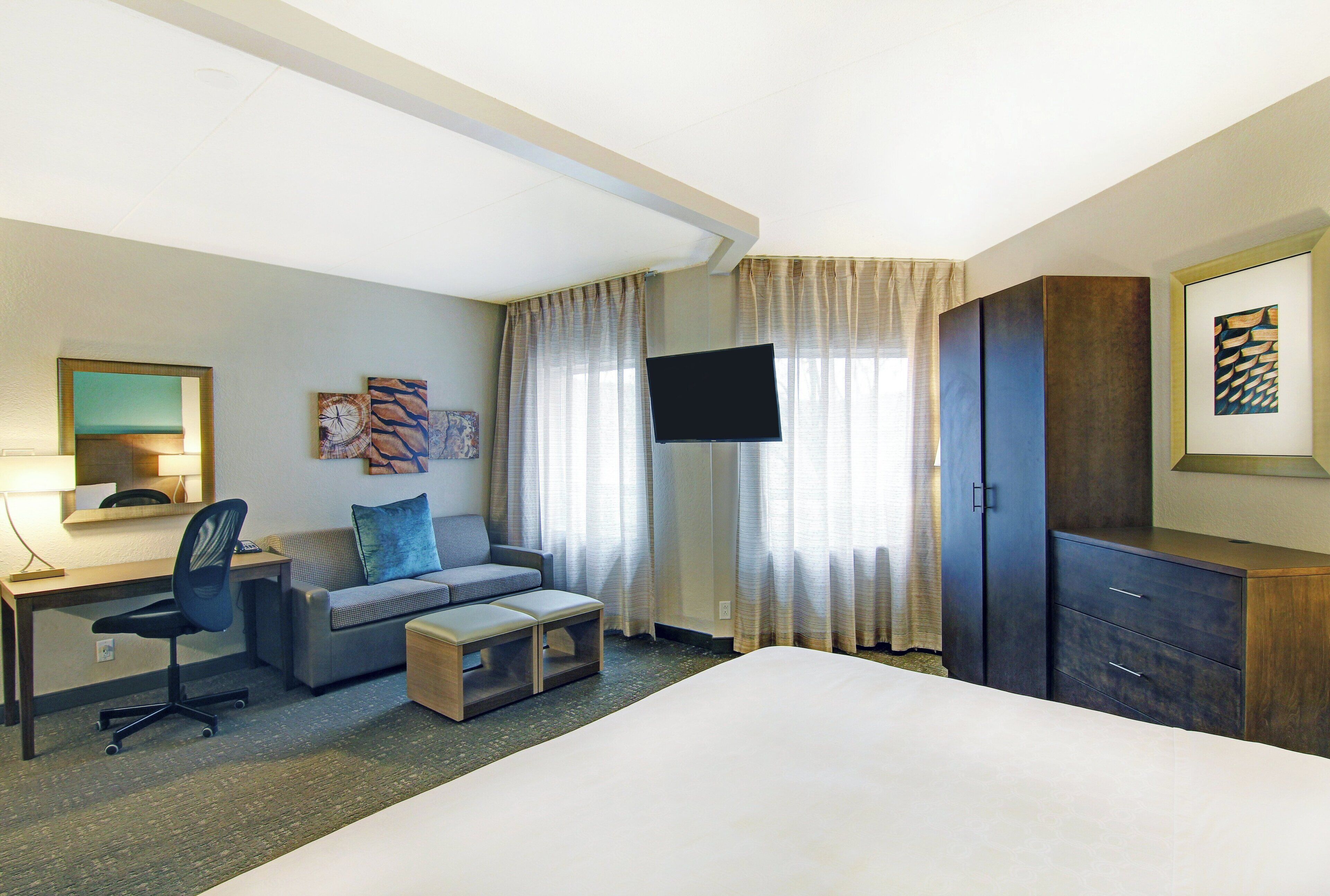 Quarto de hotel com cama, escrivaninha, poltrona, sofá, televisão e guarda-roupa.