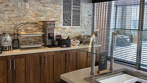 Una cocina con pared de piedra, una cafetera, una vitrina de alimentos y una ventana con persianas.