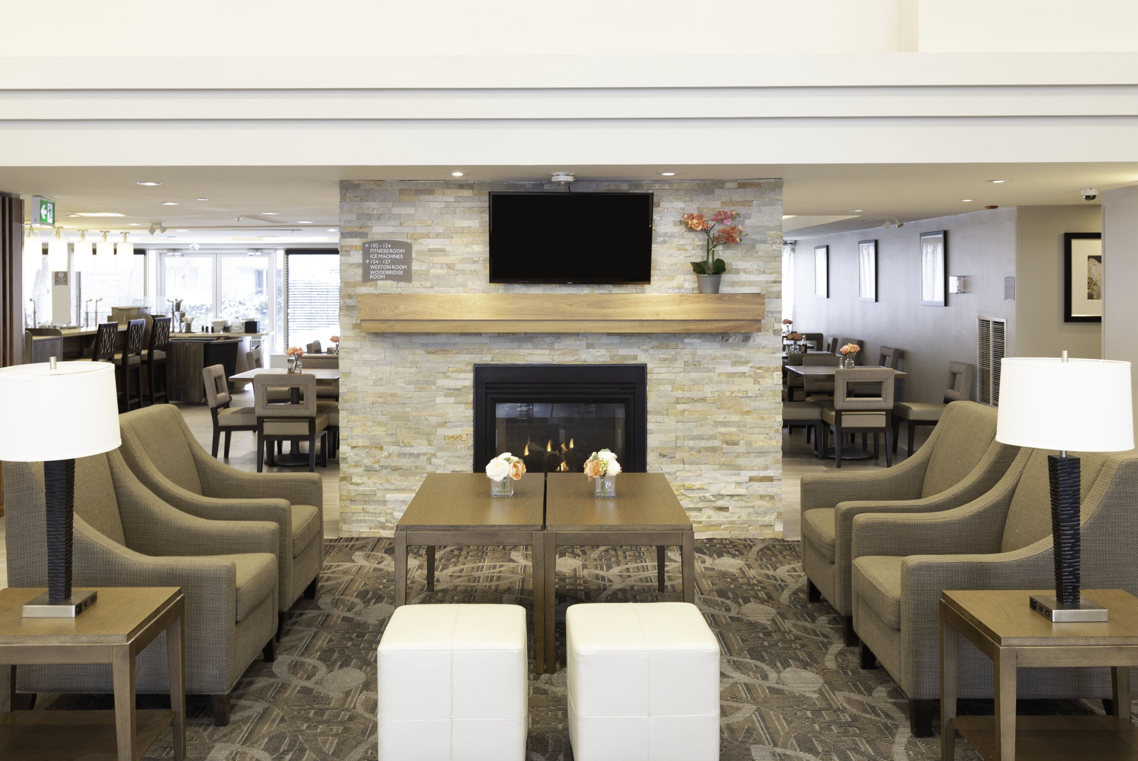 A hotel lobby with a stone fireplace, two sofas, a coffee table, and a television mounted on the wall.