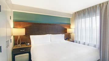 Une chambre d’hôtel avec un grand lit, deux lampes de chevet, une table de chevet, un téléphone et une fenêtre avec des rideaux.