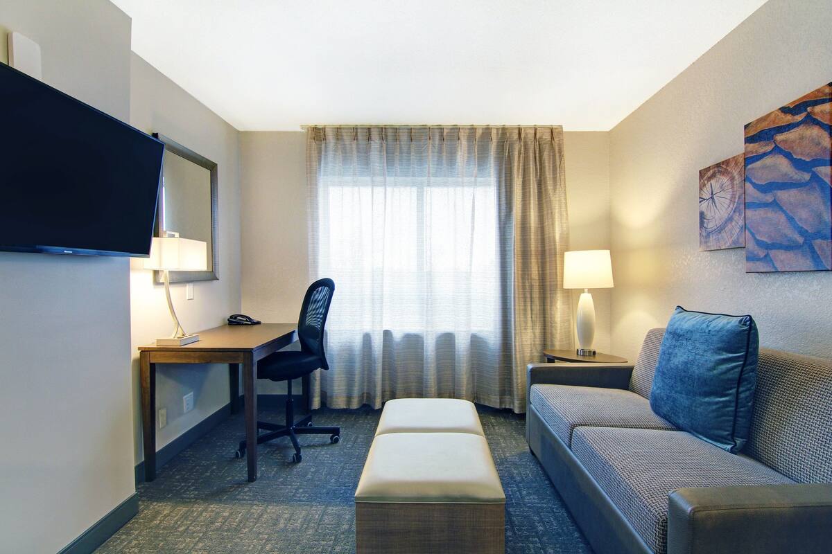 Une chambre d’hôtel équipée d’un bureau, d’une chaise, d’un canapé et d’un téléviseur fixé au mur.