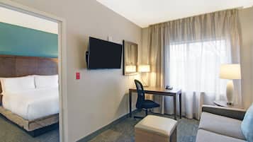 A hotel room with a bed, a desk, a chair, a TV, and a window with curtains.