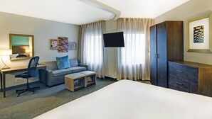 Habitación de hotel con cama, escritorio con silla, sofá, televisión y armario.