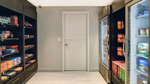 A narrow hallway with shelves stocked with snacks and beverages, a white door, and a refrigerator on the right. - Staybridge Suites Toronto - Vaughan South by IHG (Vaughan)