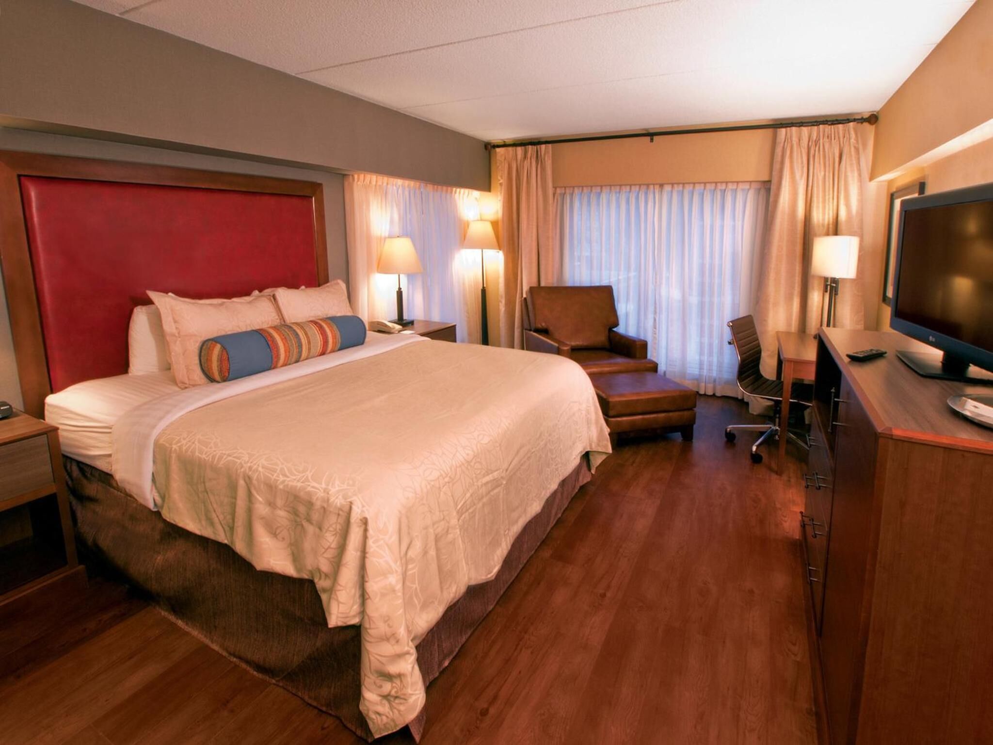 Ein Hotelzimmer mit einem großen Bett, einem Schreibtisch mit Fernseher, einem Sessel und einer Schreibtischlampe.