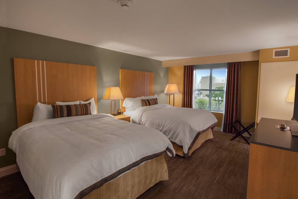 A hotel room with two beds, a desk, and a window with a view.