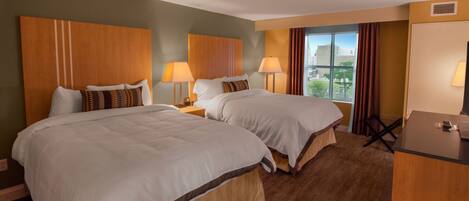 A hotel room with two beds, a desk, and a window with a view.