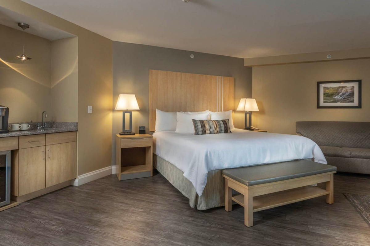 A hotel room with a bed, bedside tables, a bench, a sofa, a coffee machine, and a picture on the wall.