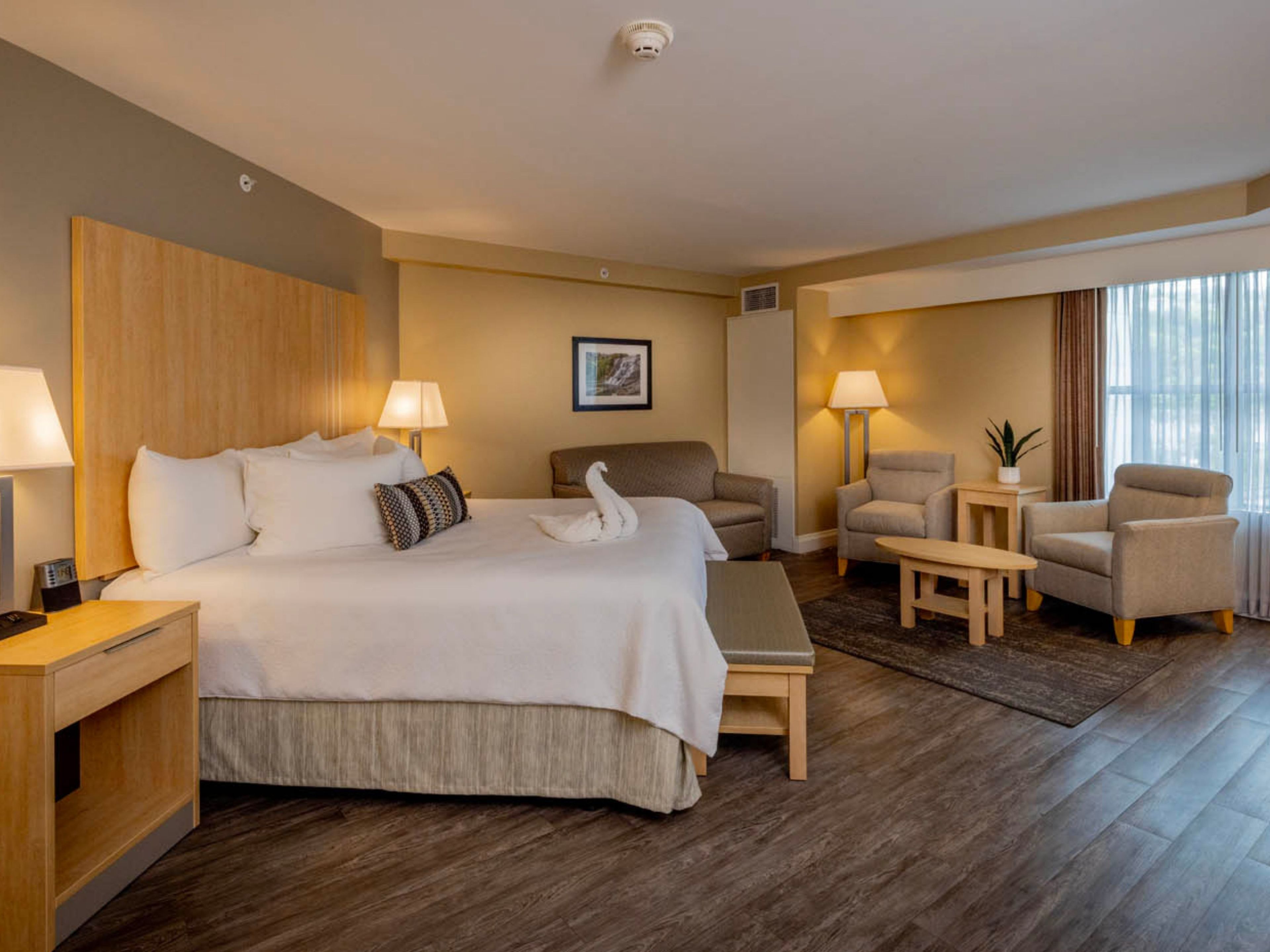 A hotel room with a bed, two armchairs, a sofa, a small table, and a lamp.