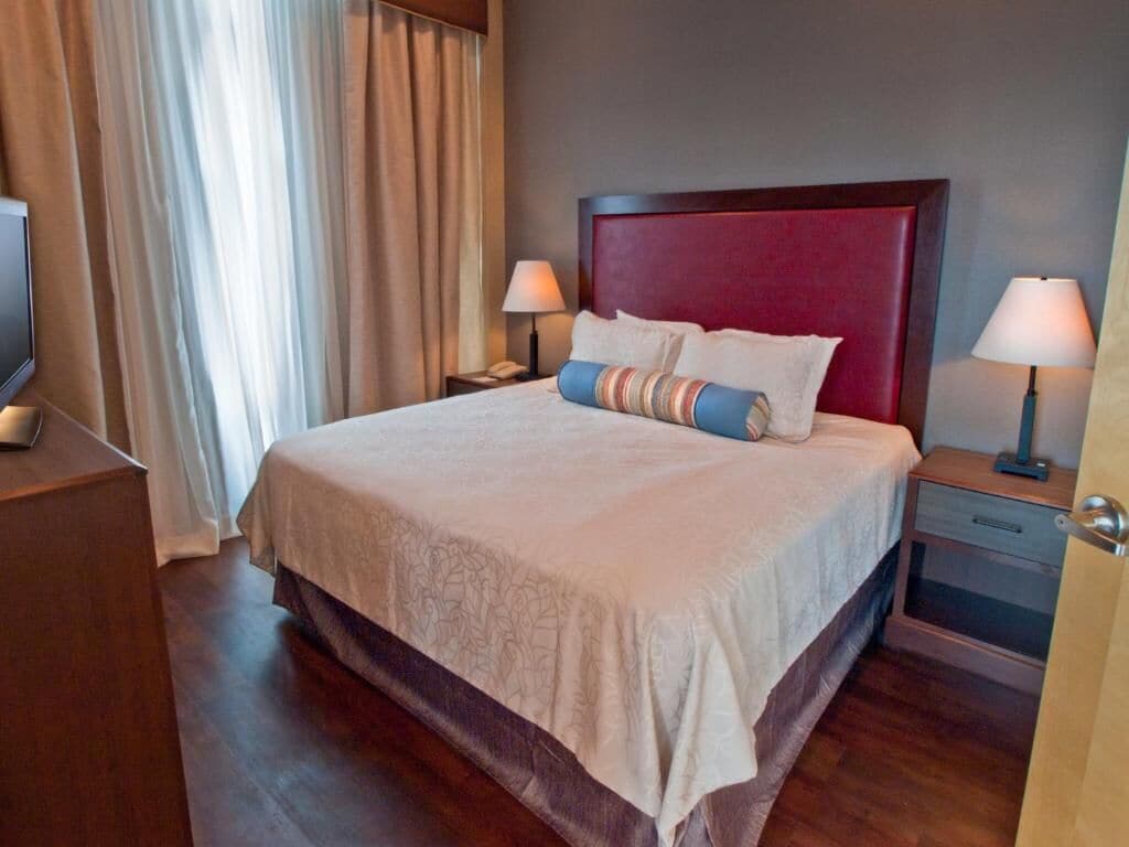 Une chambre d’hôtel avec un grand lit, deux tables de chevet avec des lampes, une télévision et des rideaux.