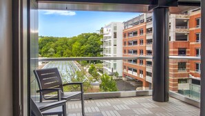 Un balcon doté d’un plancher en bois et de deux chaises, offrant une vue sur un paysage urbain avec des bâtiments et de la verdure.