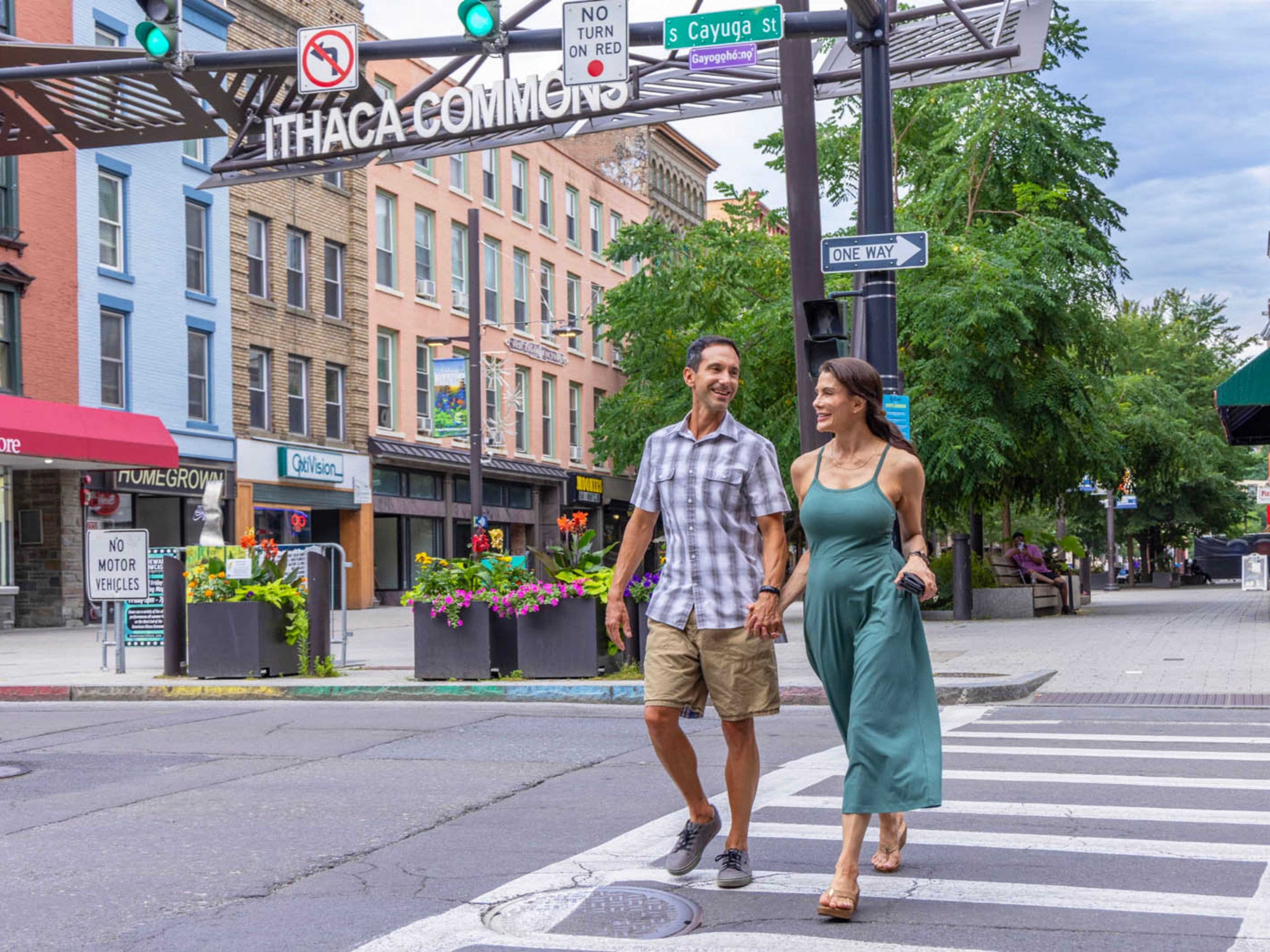 A street scene with pedestrians crossing at a crosswalk, traffic signs, and storefronts.