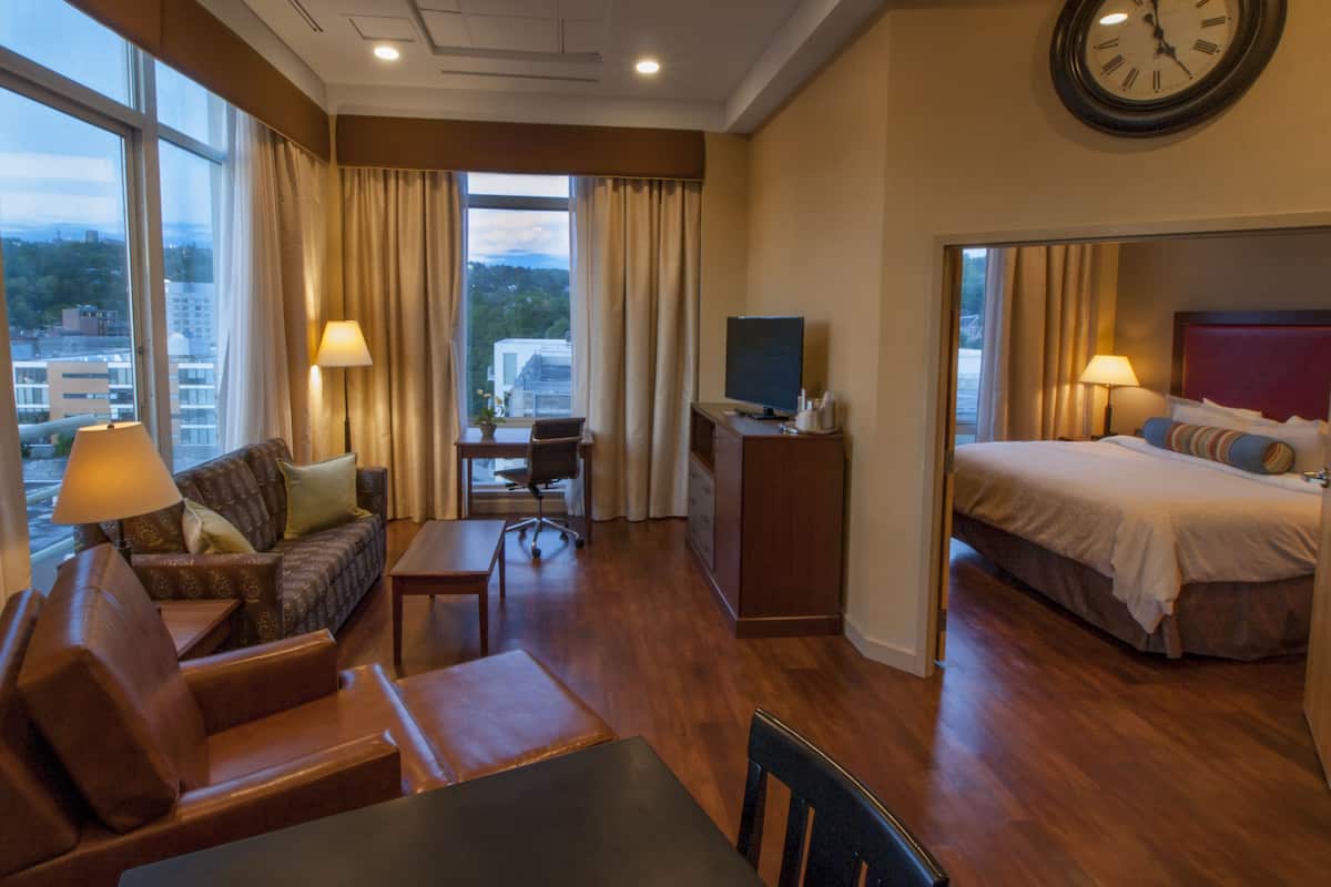 A hotel room with a bed, a desk, a TV, a sofa, and a view of the city.