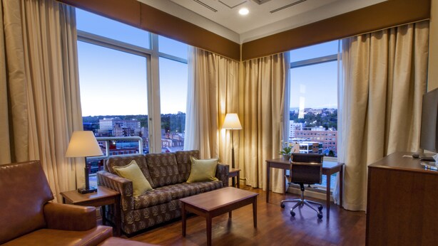 Une chambre d’hôtel équipée d’un canapé, d’un bureau, d’une chaise et offrant une vue sur le paysage urbain grâce à de grandes fenêtres.