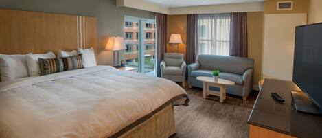 A hotel room with a large bed, a sofa, a small table, a TV, and a window with curtains.